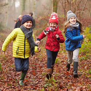 Vier Kinder in bunten Winterjacken laufen durch den Wald.